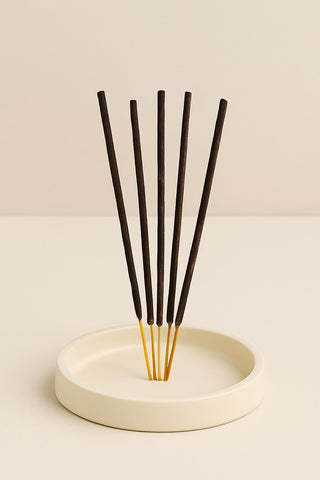 Natural incense sticks neatly arranged on a round cream-colored ceramic dish  set against a warm beige background.
